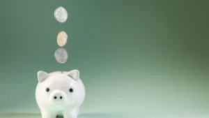 Moedas caindo dentro de um cofrinho branco