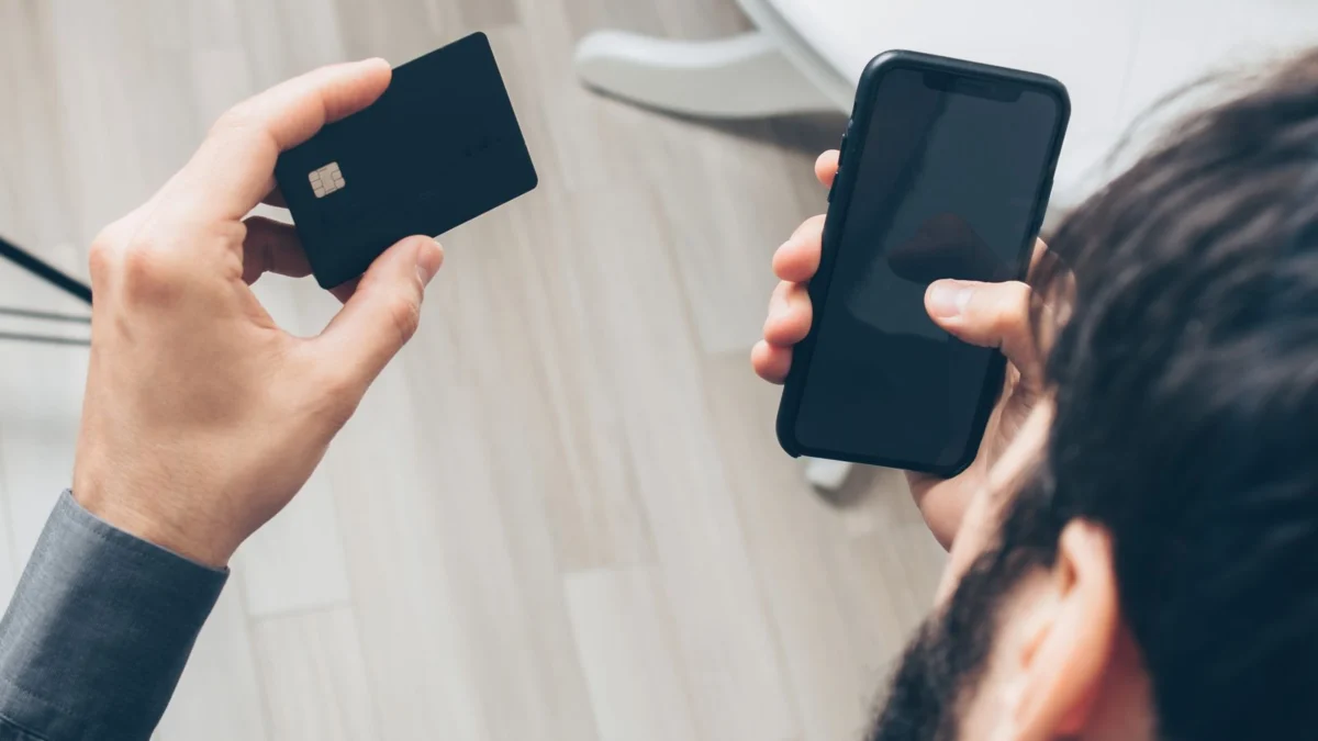 Homem segurando celular e cartão de crédito para pagar online