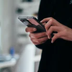Pessoa segurando um smartphone preto com as duas mãos