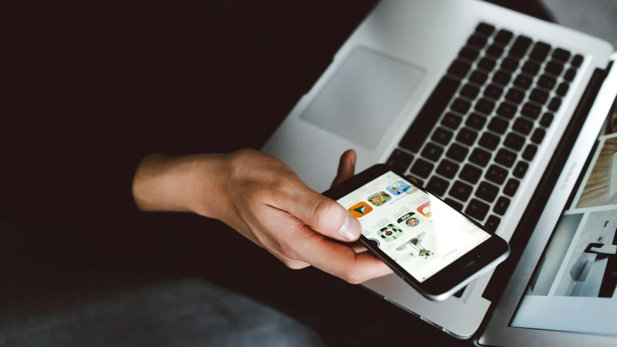 Pessoa segurando o smartphone ao lado de um notebook aberto