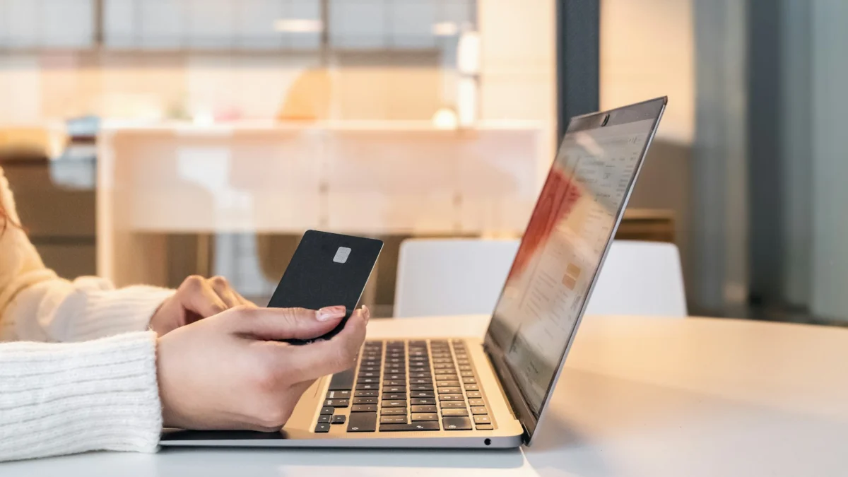 Mulher sentada em frente ao notebook segurando o celular enquanto compara preços