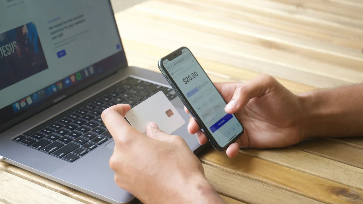 Pessoa usando smartphone e cartão de crédito em frente ao notebook para pagar uma compra online
