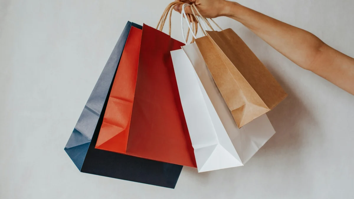 Mão segurando sacolas de compras coloridas contra um fundo branco
