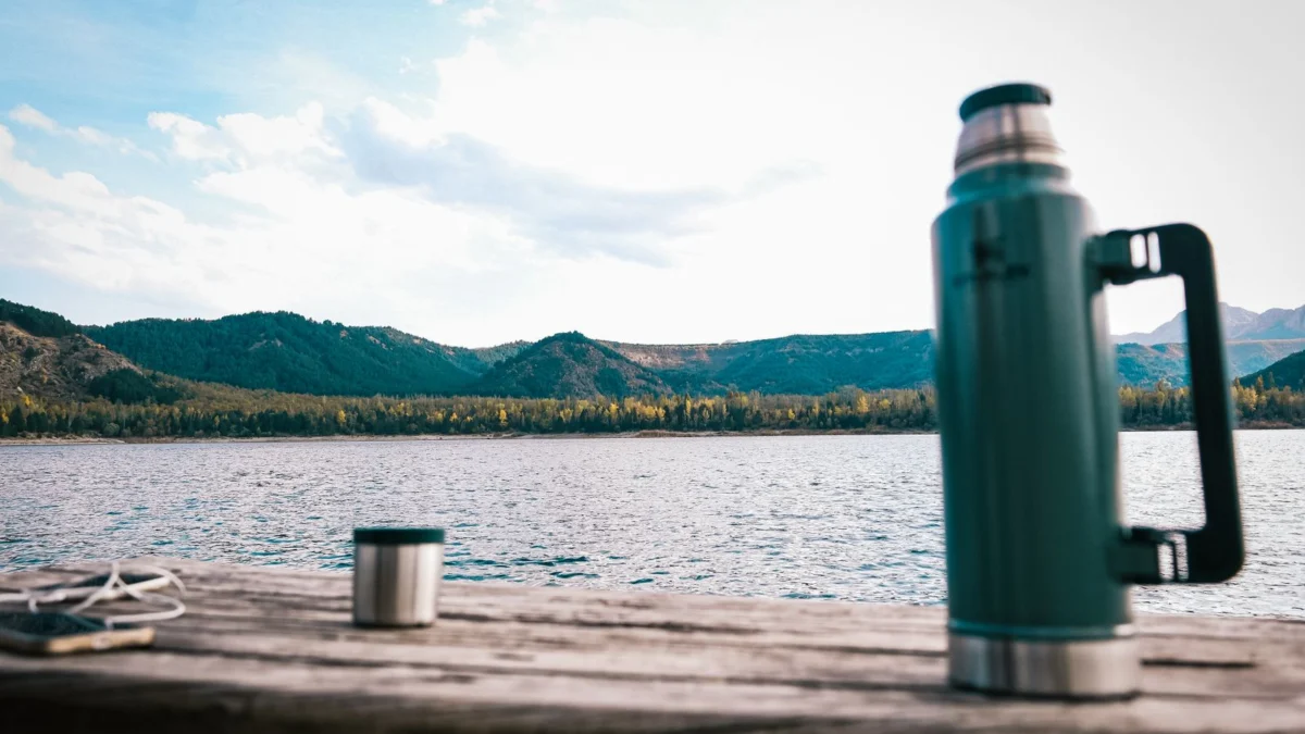 Garrafa térmica e caneca ao ar livre com lago e montanhas ao fundo