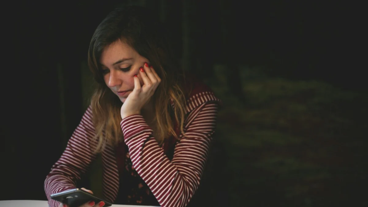 Mulher apoiada na mesa enquanto confere uma mensagem no smartphone