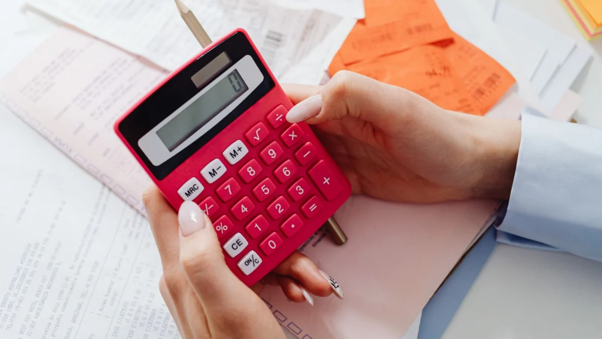 Mãos segurando uma calculadora vermelha entre recibos e documentos