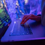 Mãos digitando em um notebook com gráficos de segurança digital na tela