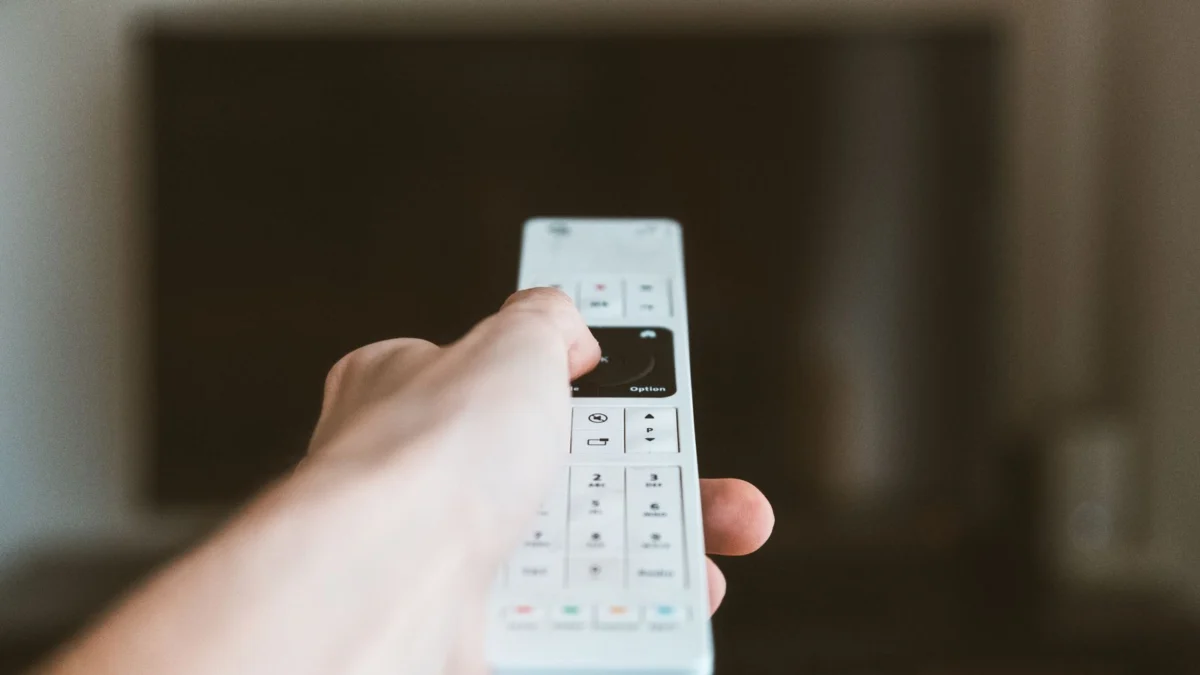 Mão usando o controle remoto na frente da TV